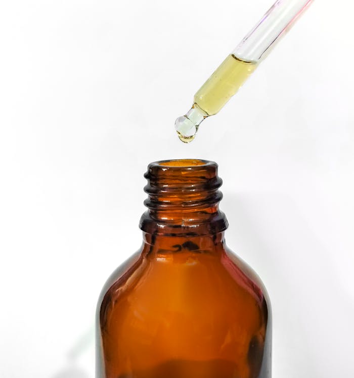 Close-up of an amber glass bottle with dropper pipette dispensing liquid.